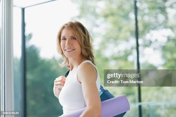 mujer sonriente sosteniendo una estera de yoga - sports clothing fotografías e imágenes de stock