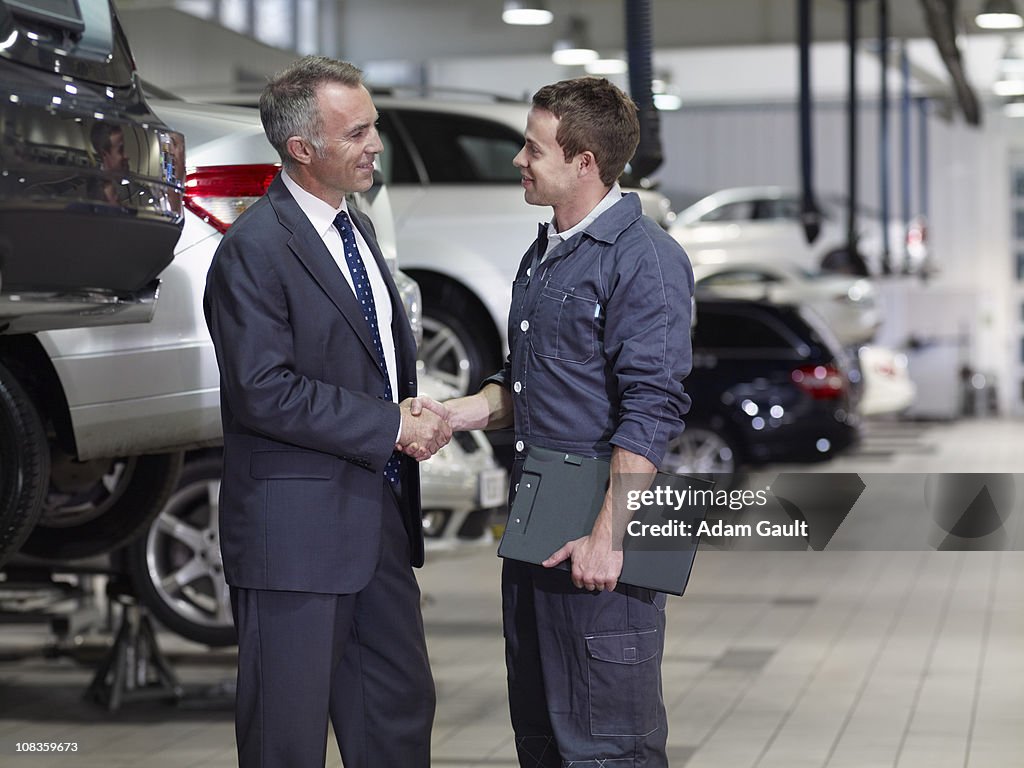 Businessman shaking hands with mechanic in auto repair shop