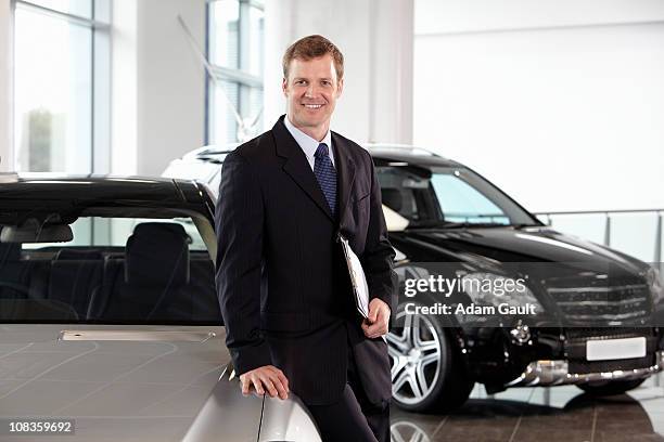 salesman leaning on new car in showroom - car salesman stock pictures, royalty-free photos & images