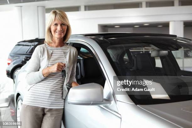 woman leaning against new car in showroom - boomers car stock pictures, royalty-free photos & images