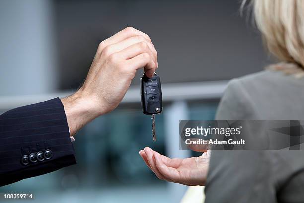 salesman handing woman car keys in automobile showroom - car salesman stock pictures, royalty-free photos & images