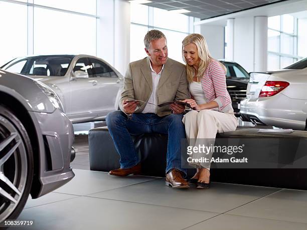 couple looking at brochure in automobile showroom - adam gault stock pictures, royalty-free photos & images