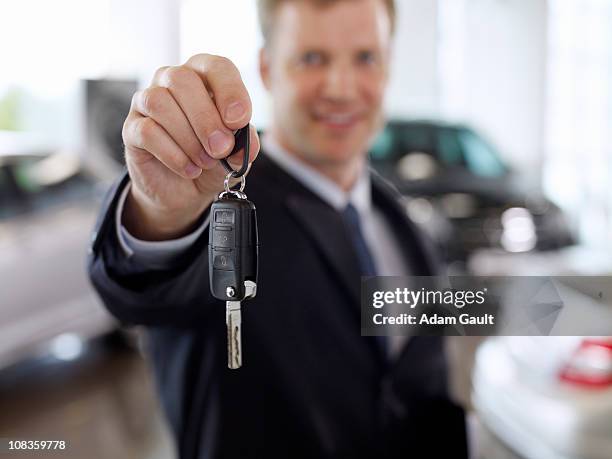 salesman holding out car key in automobile showroom - car dealership stock pictures, royalty-free photos & images