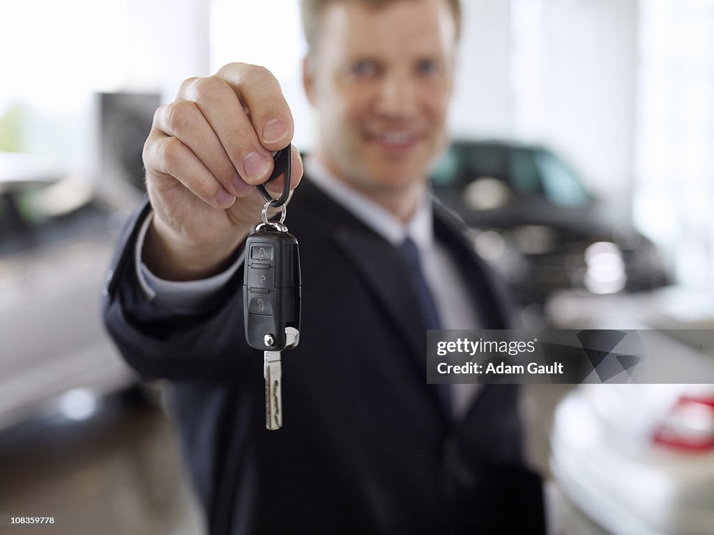 Salesman holding out car key in automobile showroom