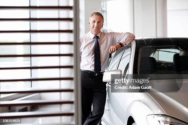 salesman leaning on new car in showroom - dealer foto e immagini stock