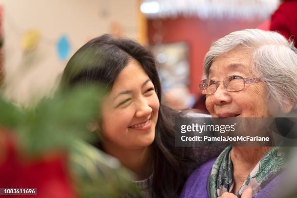 asian grandmother and mixed-ethnic granddaughter enjoying christmas celebration together - retirement community stock pictures, royalty-free photos & images