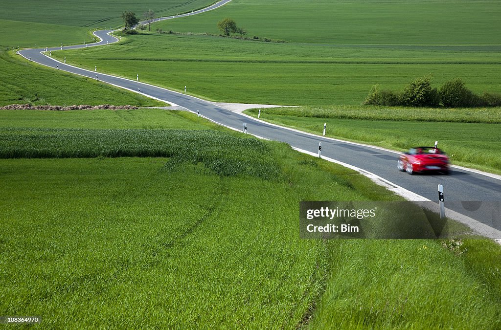 Red Sports Car Speeding on Rural Winding Road in Spring