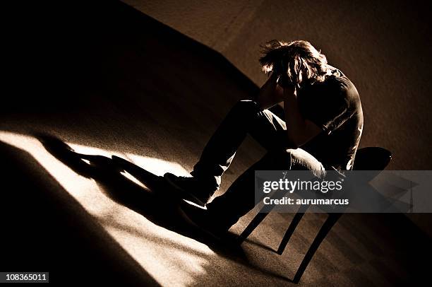 moody monotone shot of a depressed person slumped in chair - drug rehab stockfoto's en -beelden