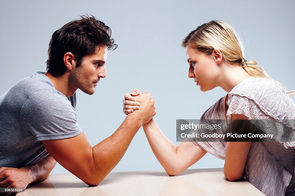Young couple arm wrestling against grey background