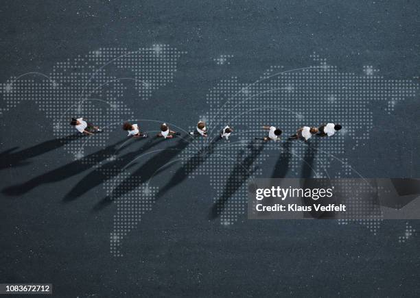 school children in uniforms walking in row across world map - global village stock-fotos und bilder