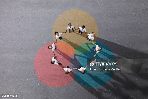 school children in uniforms holding hands while standing on painted venn diagrams - 9 circle diagram stock pictures, royalty-free photos & images