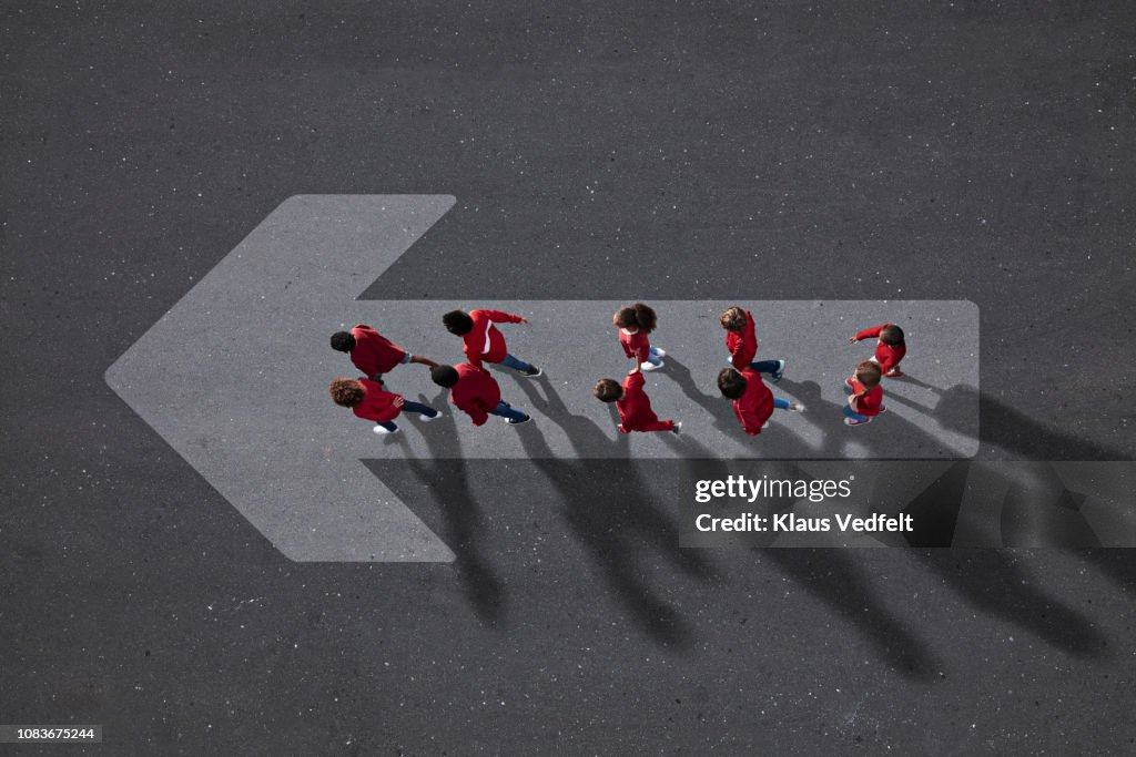 School children dressed in red, walking across big painted arrow