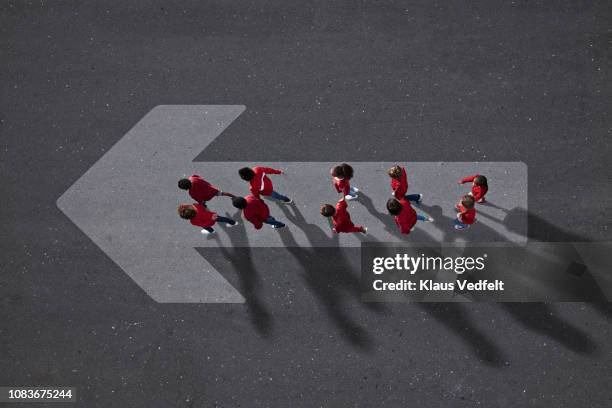 school children dressed in red, walking across big painted arrow - improvement ahead sign stockfoto's en -beelden