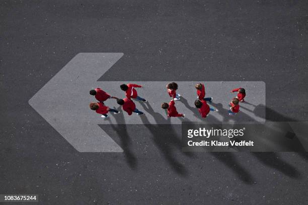 school children dressed in red, walking across big painted arrow - better future stock pictures, royalty-free photos & images