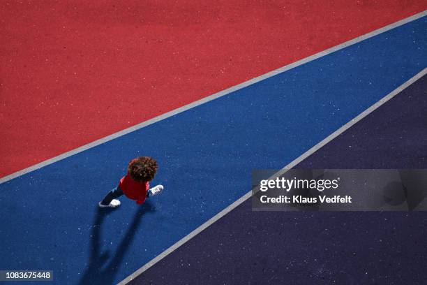 child dressed in red, walking across red and blue painted asphalt - entreprendre photos et images de collection