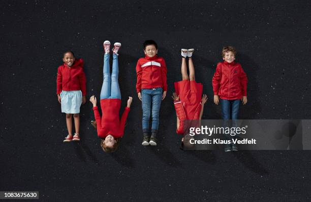 group of children dressed in red, laying on dark asphalt surface - solo bambini foto e immagini stock