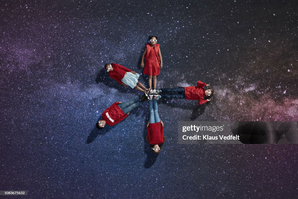 Group of children dressed in red laying on painted star background, wearing 3-D glasses