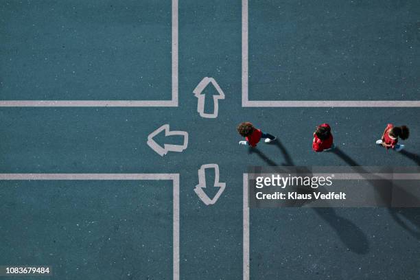children dressed in red approaching painted crossroad with arrows - follow the leader stock pictures, royalty-free photos & images
