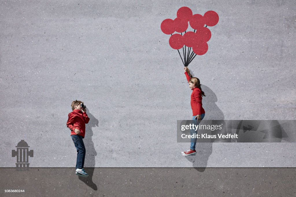 Boy photographing girl holding imaginary painted ballons