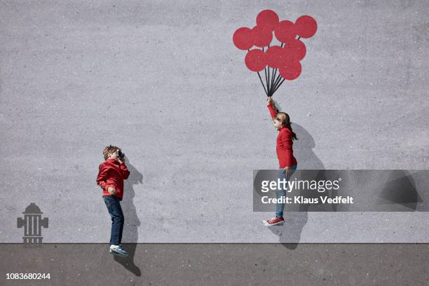 boy photographing girl holding imaginary painted ballons - evasión fotografías e imágenes de stock