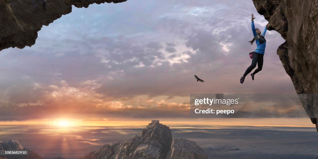 Woman Free Climbing Sheer Rock Face High Up At Sunrise