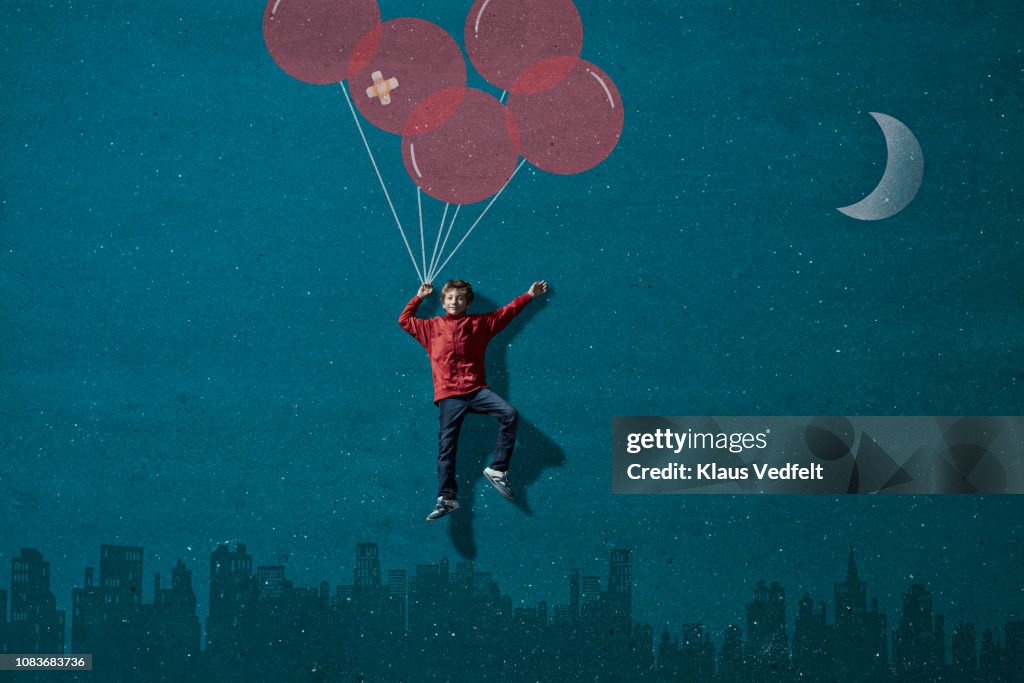 Boy wearing VR goggles holding painted imaginary balloons flying above skyline
