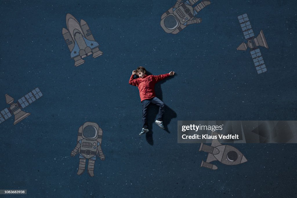 Boy laying on painted imaginary background among space travel objects