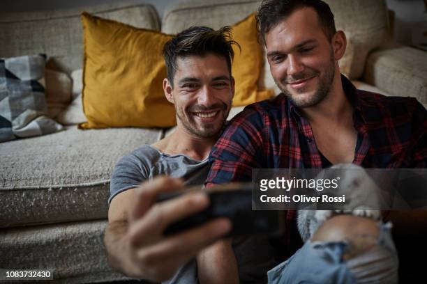 smiling gay couple taking a selfie with kitten at home - cat selfie stock-fotos und bilder