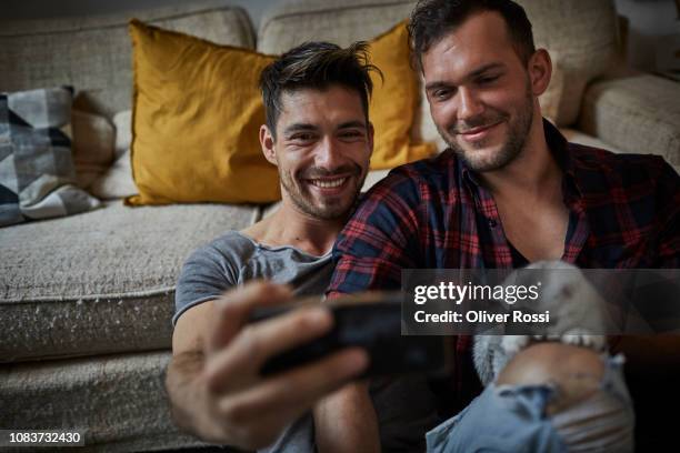 smiling gay couple taking a selfie with kitten at home - cat selfie stock pictures, royalty-free photos & images