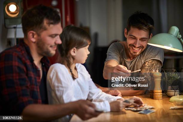 Two men playing cards with girl at table at home
