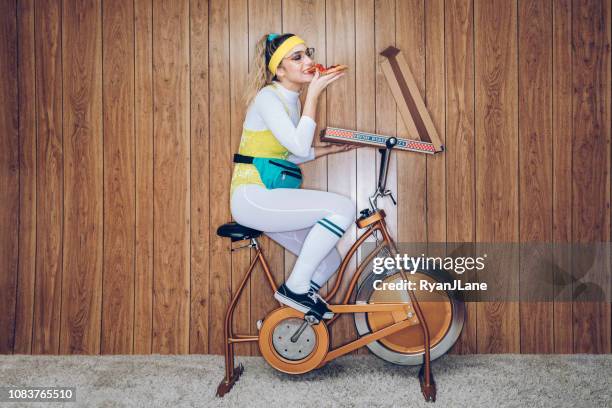 retro style exercise bike woman eighties era eating pizza - bicicleta vintage imagens e fotografias de stock