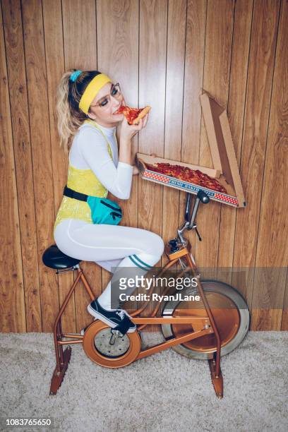 retro style exercise bike woman eighties era eating pizza - sweet bizarre vintage rides imagens e fotografias de stock