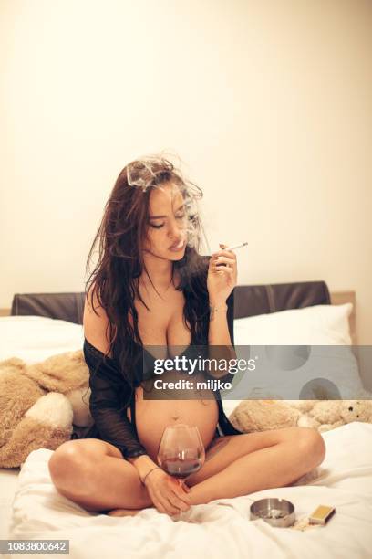 pregnant woman sitting on bed and has some unhealthy habits - alcohol and smoking stock pictures, royalty-free photos & images