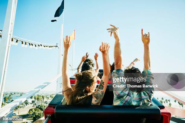 rear view of couple with arms raised about to begin descent on roller coaster in amusement park - eccitazione foto e immagini stock