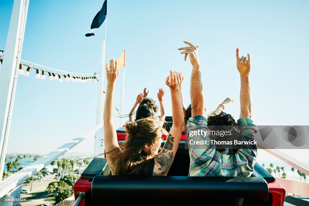 Rear view of couple with arms raised about to begin descent on roller coaster in amusement park
