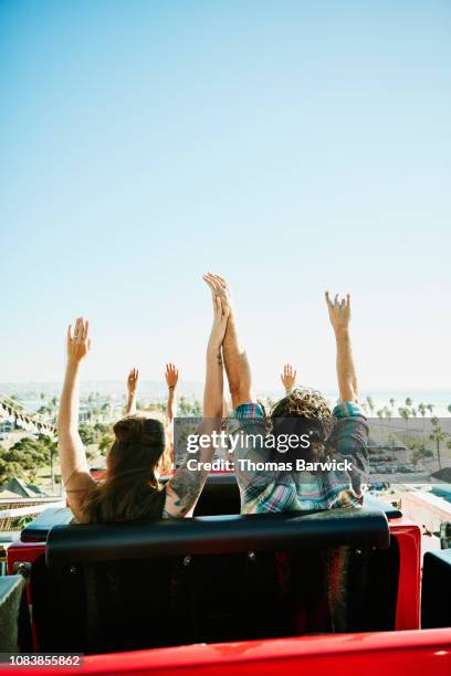 rear view of couple with arms raised beginning descent on roller coaster in amusement park - achtbaan stockfoto's en -beelden