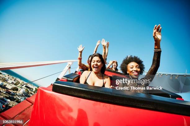 friends screaming and laughing while riding roller coaster at amusement park - achterbahn stock-fotos und bilder