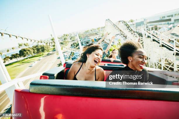 laughing and smiling friends riding roller coaster at amusement park - anticipation rollercoaster stock pictures, royalty-free photos & images