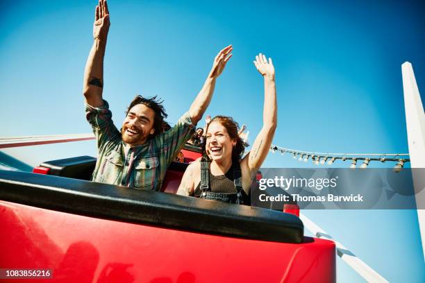 laughing couple with arms raised riding roller coaster - amusementsparkritje stockfoto's en -beelden