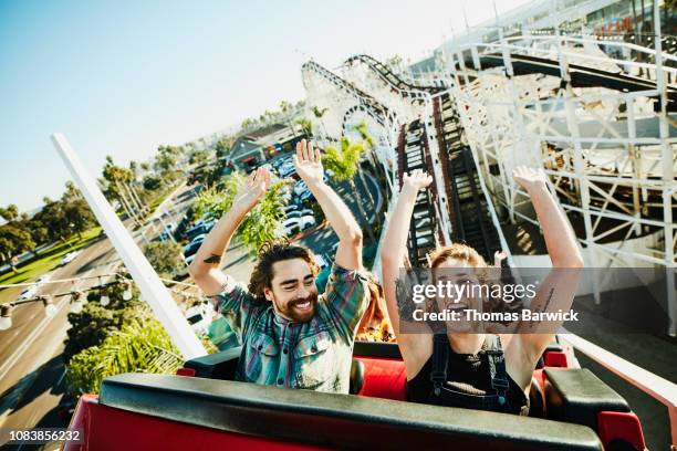 laughing couple with arms raised riding roller coaster at amusement park - woman look straight black shirt stock pictures, royalty-free photos & images