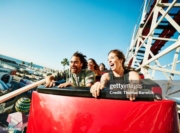 laughing and screaming couple riding roller coaster at amusement park - achtbaan stockfoto's en -beelden