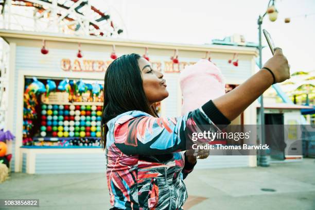 smiling woman taking selfie with smart phone while holding cotton candy during visit to amusement park - american influencer - fotografias e filmes do acervo