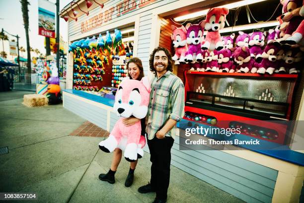 smiling couple holding stuffed animal after winning carnival game at amusement park - traveling carnival stockfoto's en -beelden