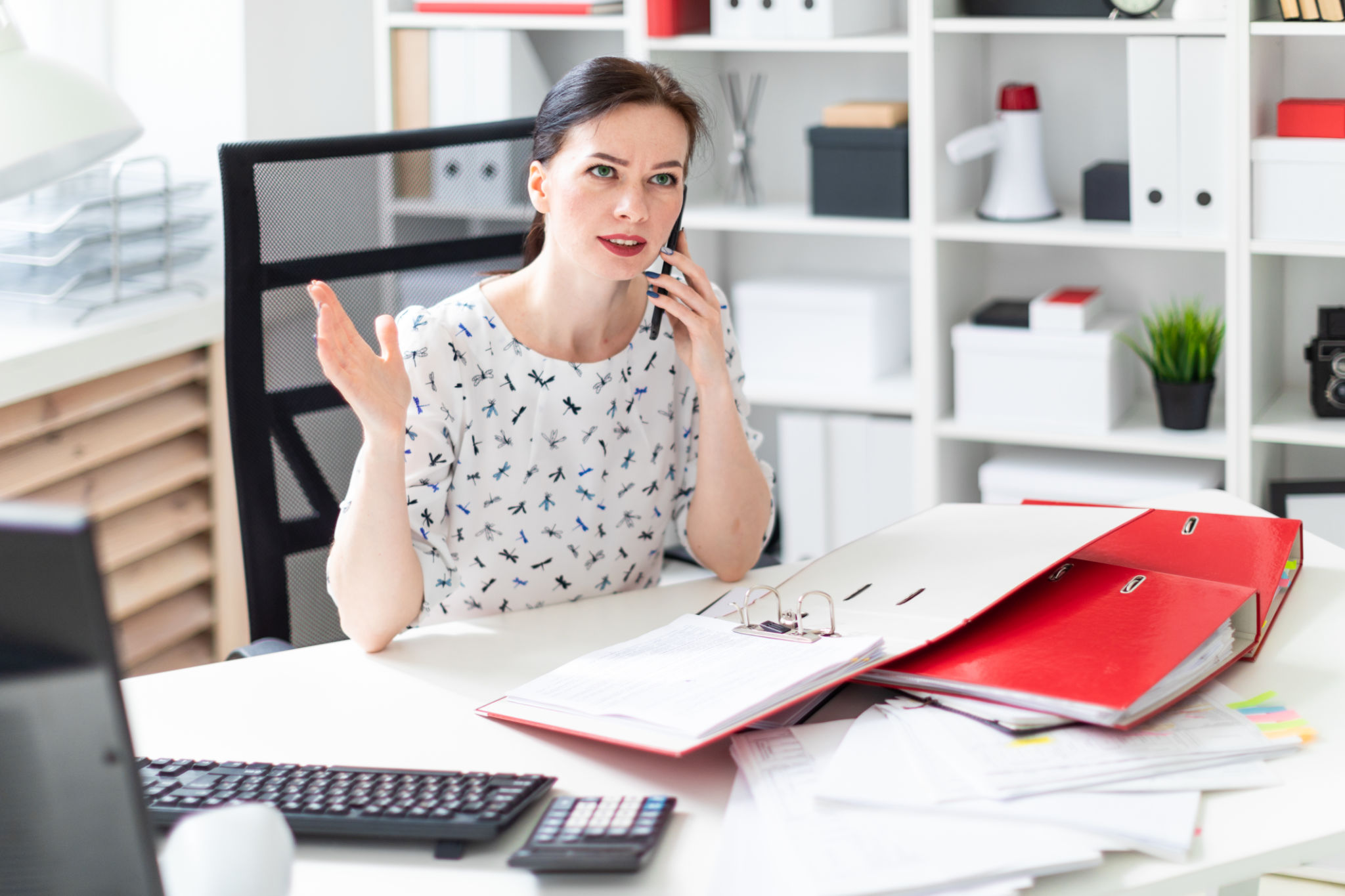 A young girl sitting in the office at the computer Desk, working with documents and talking on the phone. A young girl sitting in the office at the computer Desk, working with documents and talking on the phone.