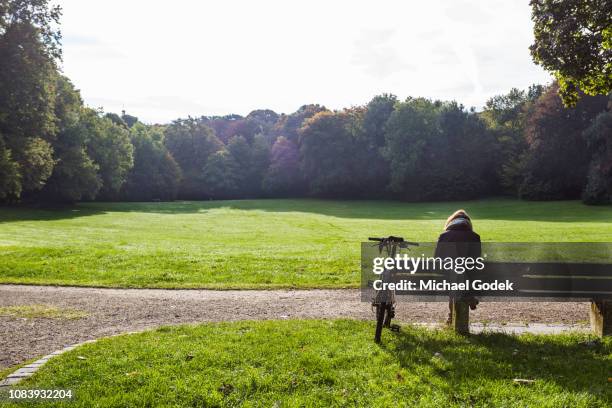 female cyclist relaxing on bench at bavaria park - park bench stock-fotos und bilder