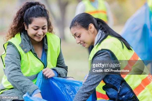 two female friends enjoy volunteering together - volunteers cleaning public park stock pictures, royalty-free photos & images