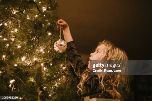 little girl decorating christmas tree with ornaments - christmas tree decorations imagens e fotografias de stock