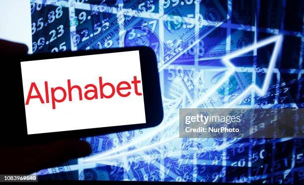 The logo of Alphabet is seen on a screen of a smartphone next to a screen with an illustration ofthe stock market. Alphabet is listed in Nasdaq. The...