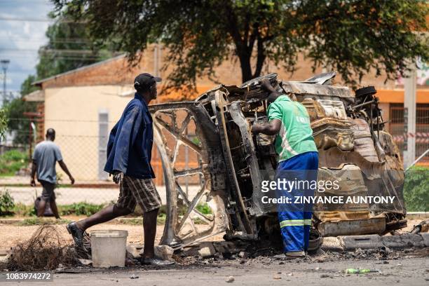 Scrap metal collectors salvages sellable parts from a car shell burnt during the three days protests in Emakhandeni township, in Bulawayo, on January...