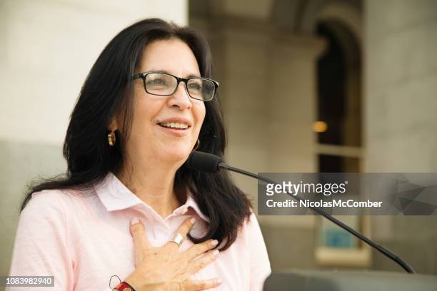 mature latina woman touched by crowd reaction during speech over microphone - acceptance speech stock pictures, royalty-free photos & images